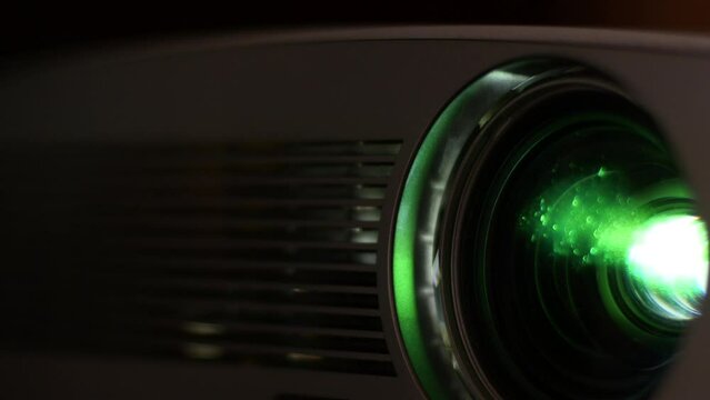 The lens of a movie projector emits multi-colored light to show slides, a movie or a video clip. Leisure, home theater, business presentation.