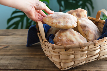 Woman's hands placing pita bread in wooden basket on a table. Copy space.
