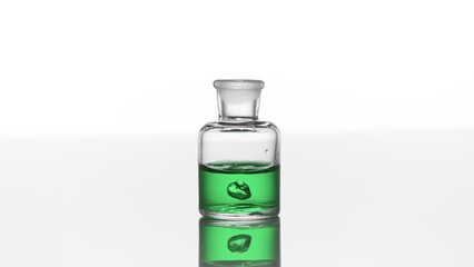 Drop of eucalyptus oil falls down into clear old fashioned bottle with green transparent liquid on...