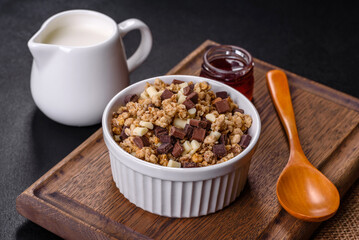 Tasty healthy breakfast with cereals, granola, chocolate, milk and jam on a dark concrete background