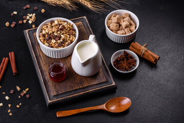 Tasty healthy breakfast with cereals, granola, chocolate, milk and jam on a dark concrete background