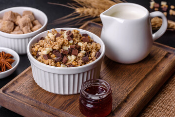 Tasty healthy breakfast with cereals, granola, chocolate, milk and jam on a dark concrete background