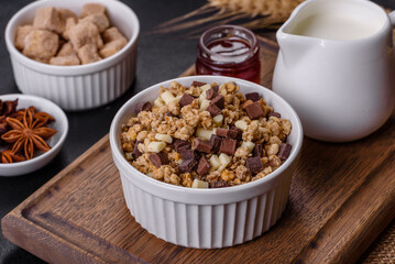 Tasty healthy breakfast with cereals, granola, chocolate, milk and jam on a dark concrete background