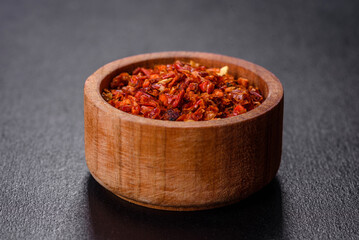 Red crushed paprika in a wooden dish on a dark concrete background