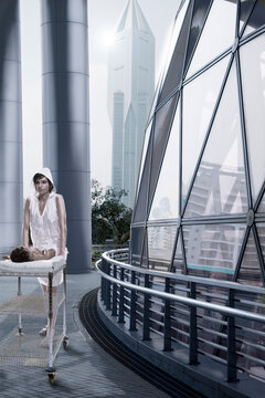 Young Woman With Newborn Baby On Rolling Cart Walking Outside Next To Geodesic Dome Architecture 