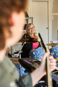 View of Drummer over guitar players shoulder in garage band composed of middle aged women, practicing in residential garage 