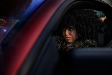 Young African American woman in a sports car looking straight ahead with a mischievous expression. 