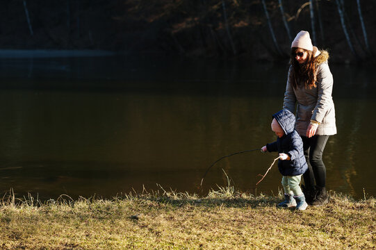 Mother with daughter fishing with a stick in pound at early spring park.