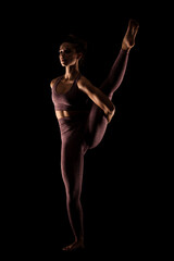 Fototapeta na wymiar Fit woman practicing yoga poses. Side lit half silhouette girl doing exercise in studio against black background..