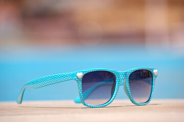 Closeup of blue sunglasses on swimming pool side at tropical resort on warm sunny day. Summer...