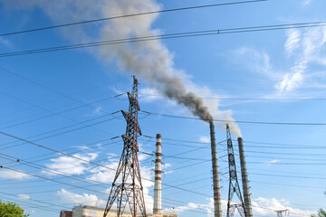 High voltage electric pylons against coal power plant high pipes with black smoke moving upwards polluting atmosphere. Production of electrical energy with fossil fuel concept