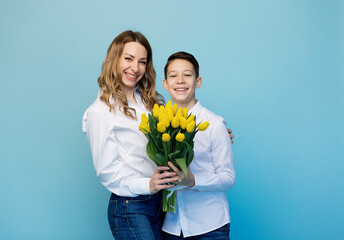 A happy smiling mother with tulips hugs her son in gratitude, smiles and looks at the camera. There...