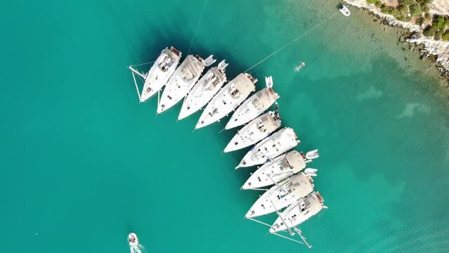 Segelboote als Flotille beim Ankern im P&auml;ckchen nahe Ufer in Griechenland in blauem Meer im Urlaub bei Sonne per Drohne als Luftaufnahme gefilmt