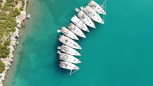 Segelboote als Flotille beim Ankern im P&auml;ckchen nahe Ufer in Griechenland in blauem Meer im Urlaub bei Sonne per Drohne als Luftaufnahme gefilmt