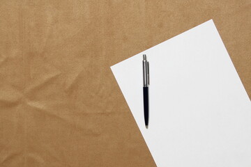 Template of white paper with pen lies diagonally on light brown cloth background. Concept of business plan and strategy. Stock photo with empty space for text and design.