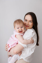 Sweet young mother holding her little 1-year-old daughter in hands.
Caring brunette woman laying with her baby child at home. Tenderness and love between mother and daughter. Lovely family indoors.