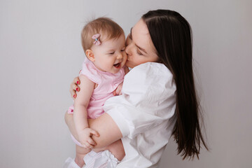 Sweet young mother holding her little 1-year-old daughter in hands.
Caring brunette woman laying with her baby child at home. Tenderness and love between mother and daughter. Lovely family indoors.