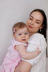 Sweet young mother holding her little 1-year-old daughter in hands.
Caring brunette woman laying with her baby child at home. Tenderness and love between mother and daughter. Lovely family indoors.