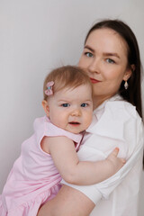 Sweet young mother holding her little 1-year-old daughter in hands.
Caring brunette woman laying with her baby child at home. Tenderness and love between mother and daughter. Lovely family indoors.