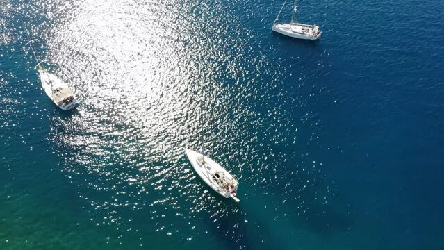 Segelboote als Flotille beim Ankern in Griechenland in blauem Meer im Urlaub bei Sonne per Drohne als Schwenk gefilmt