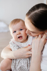 Sweet young mother playing with her little 1-year-old daughter.
Caring brunette woman embracing her small child in her arms. Tenderness and love between mother and daughter. Lovely family indoors.