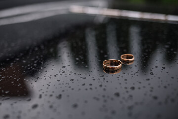 Two wedding rings lie on top of each other against a dark background. Drops of water are falling on...