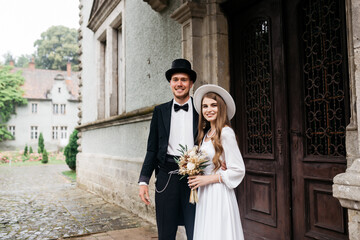 Happy young couple. Brides in hats. Young girl in a white wedding dress and hat with a bouquet of flowers. Brides in the castle. Bride and groom.