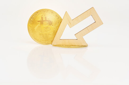 On a white surface, bitcoin and an arrow showing a decrease in the value of the cryptocurrency.