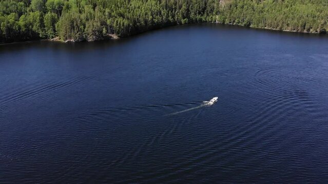 Luftaufnahme von Motorboot fahrend auf Wasser mit Wellen zwischen Inseln mit B&auml;umen in Schweden auf See bei Sonne per Drohne gefilmt