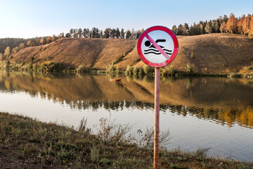 There is a no-swimming sign on the river bank. summer day