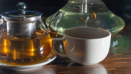 Picture of glass teapot with ceramic cup of green tea on dark background. Hot chinese green tea.