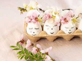 Natural white easter eggs with drawn sweet face in floral wreaths in a basket in soft light. Happy Easter, holiday card.