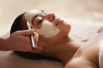 Your skin deserves some pampering. A face mask being applied to a beautiful young woman at a beauty...