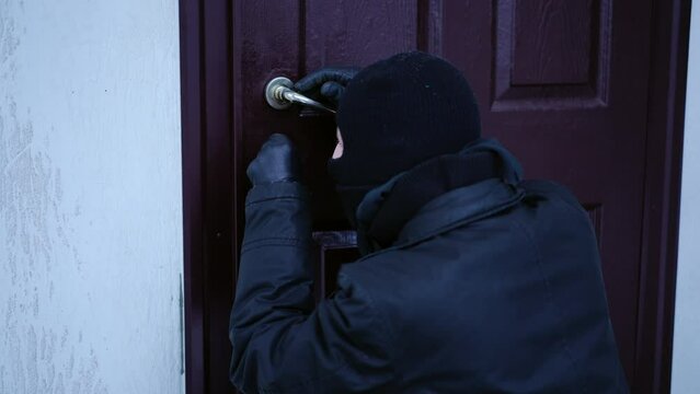 Back view thief picking the lock looking around and running away outdoors. Caucasian masked man breaking in house caught at crime scene. Law violation concept