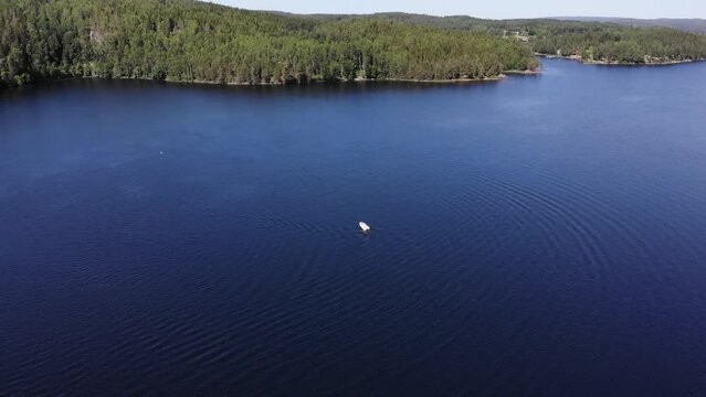 Luftaufnahme von Motorboot fahrend auf Wasser mit Wellen zwischen Inseln mit B&auml;umen in Schweden auf See bei Sonne per Drohne gefilmt
