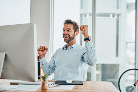 What A Victory. Shot Of A Handsome Young Businessman Doing A Fist Pump While Working On A Computer In An Office.