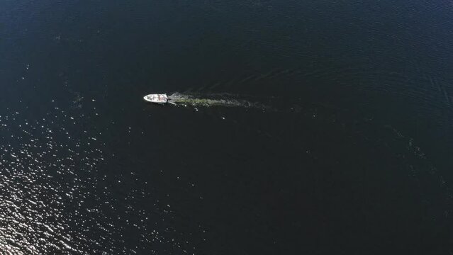 Luftaufnahme von Motorboot fahrend auf Wasser mit Wellen zwischen Inseln mit B&auml;umen in Schweden auf See bei Sonne per Drohne gefilmt