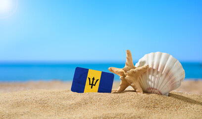 Tropical beach with seashells and Barbados flag. The concept of a paradise vacation on the beaches of Barbados. - obrazy, fototapety, plakaty