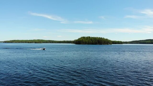 Luftaufnahme von Motorboot fahrend auf Wasser mit Wellen zwischen Inseln mit B&auml;umen in Schweden auf See bei Sonne per Drohne gefilmt
