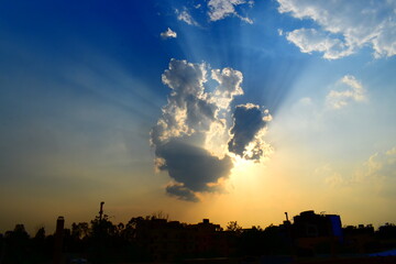 Sunrays piercing through a cluster of clouds above a natural skyline silhouette