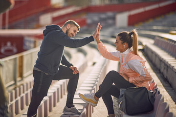 beardy guy and beautiful female giving high-five to each other at the stadium,  smiling