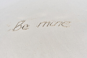 Text Be mine written on white sand of tropical beach.