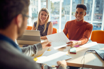 Young colleagues in a commission are taking documents from a male applicant during an interview for...