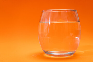 Glass tumbler with purified water on orange and light orange gradient background.