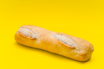 Small baguete of french bakery bread on a pure yellow surface.