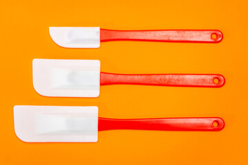 Set of three red and white kitchen spatulas made of silicone and plastic insulated on an orange surface.