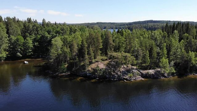 Luftaufnahme als Schwenk &uuml;ber blauen See mit Inseln und Steinfelsen mit Wald aus B&auml;umen bei Sonne im Sommer per Drohne