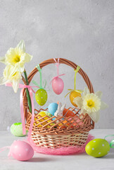 Basket with Easter bunny and colorful eggs on gray background with daffodils. Festive card