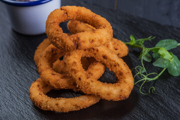 Fried onion rings in a black tray with garlic sauce