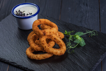 Fried onion rings in a black tray with garlic sauce